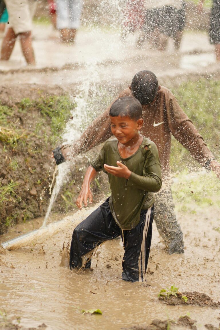 Joyful children playing in an irrigated muddy rice field during the rainy season in rural Nepal.